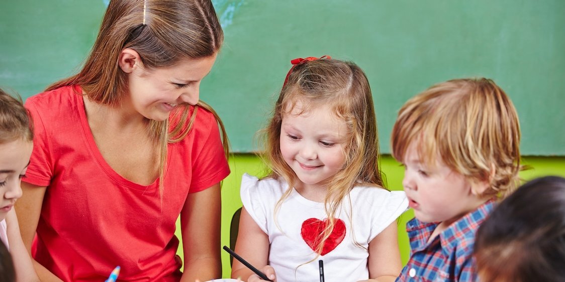 Eine Erzieherin sitzt mit Kindern am Tisch, die malen.. Artikel "Ausmalbilder rund ums Essen" öffnen.