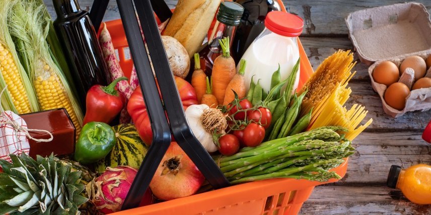 In einem roten Supermarktkorb liegen Paprika, Möhren, Mais, Tomaten, Spargel, Bohnen, Knoblauch und Spaghetti, ein Baguette, Milch, Öl, Ananas und ein Granatapfel. Daneben liegen Eier in einer Schachtel und Getränkeflaschen.. Artikel "Verbraucherpreise steigen nicht alle gleich" öffnen.