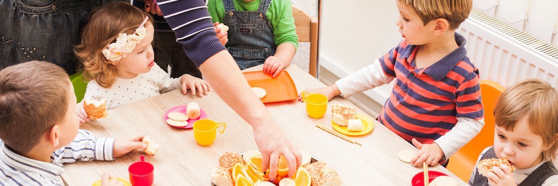 Kitakinder sitzen am Tisch und essen aufgeschnittenes Obst als Nachmittagsimbiss.