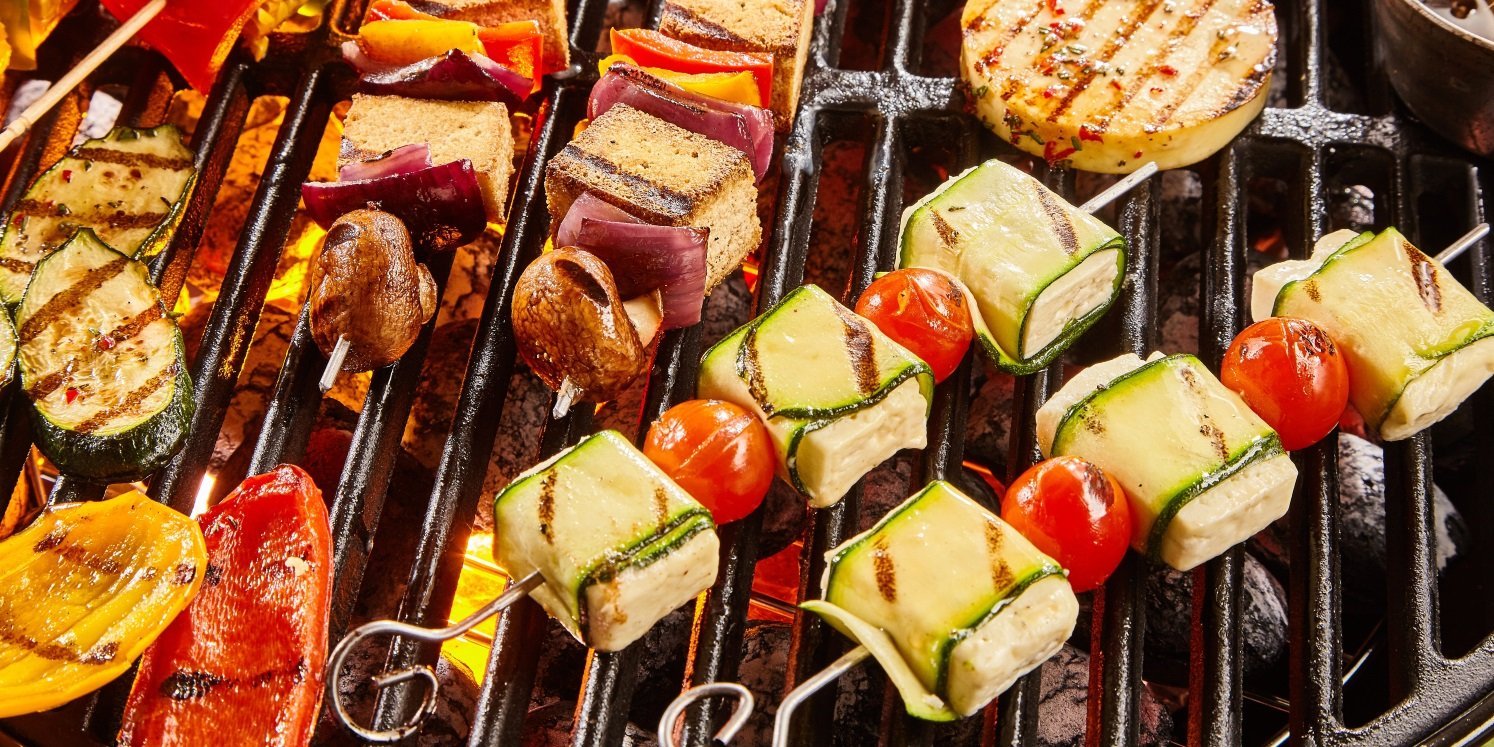 Auf einem Grillrost liegen verschiedene Spieße mit Zwiebeln, Zucchinistreifen, Fetawürfeln und Cocktailtomaten sowie einzelne Paprikastücke. . Artikel "Ruckzuck Grillideen für den Feierabend" öffnen.