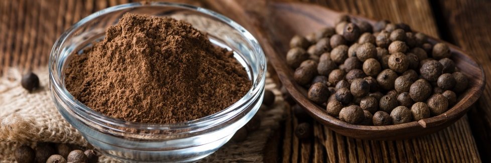 Gemahlener Pigment in einer kleinen Glasschlüssel und Pimentkörner auf einem Holzlöffel