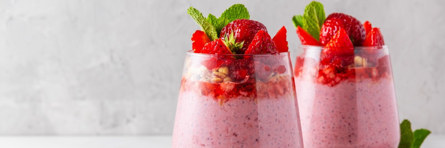 Zwei Gläser mit Erdbeerquark und frischen Erdbeeren stehen auf einer hellen Unterlage.