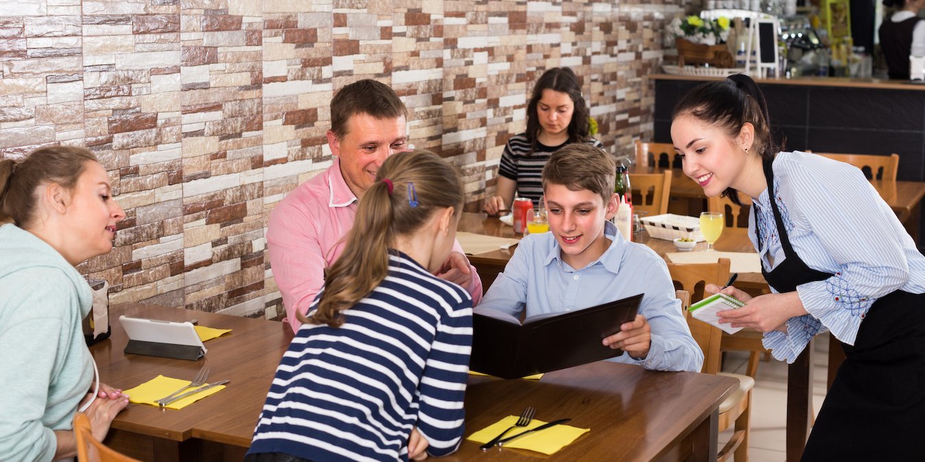 Kinder sitzen an einem Restaurant-Tisch und werden bedient.. Artikel "Unser Restaurant-Tisch" öffnen.