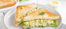 Auf einem Teller liegen Chopped Sandwiches aus Toastbrotscheiben mit Salat, Kräuter, Ei, Mayonnaise und Gurken.  