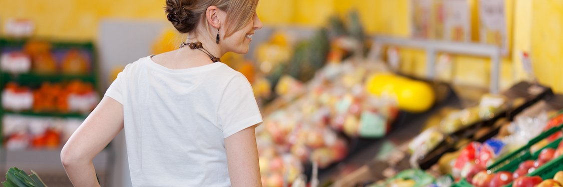 Junges Mädchen schiebt einen Einkaufwagen durch die Obst- und Gemüseabteilung eines Supermarkts.