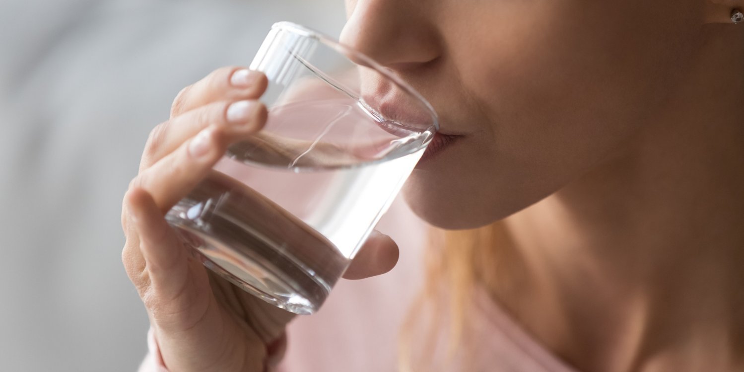 Eine Frau trinkt aus einem Glas mit Wasser.. Artikel "Wasser" öffnen.