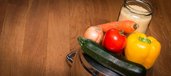 Zutaten für das Gemüsegericht auf einem Topf angerichtet: eine Zwiebel, ein Zucchino, eine Karotte, zwei Tomaten, eine Paprika und Couscous.