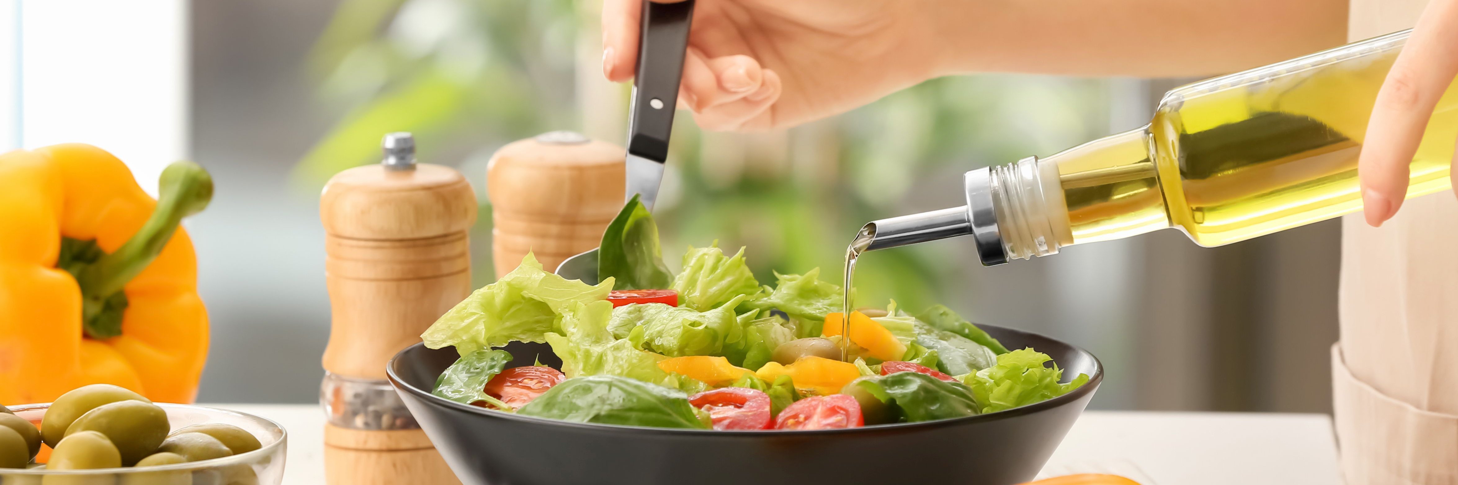 Frau gibt Öl aus Glasflasche an Blattsalat.