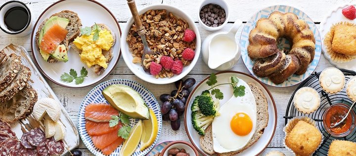 Ausschnitt eines Brunch-Buffets mit Brot, Käse, Wurst, Kaffee, Rührei, Spiegelei, Avocado, Lachs, Müsli, Himbeeren, Trauben, Marmorkuchen und Muffins.  