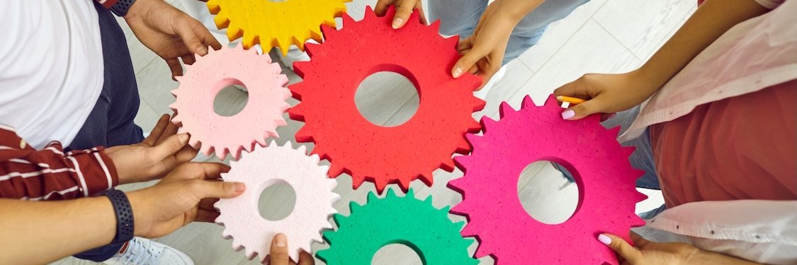 Hände von jungen Menschen verbinden bunte Zahnräder, die ineinander greifen.