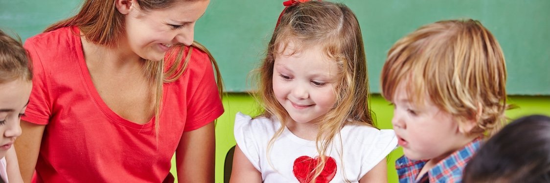 Eine Erzieherin sitzt mit Kindern am Tisch, die malen.
