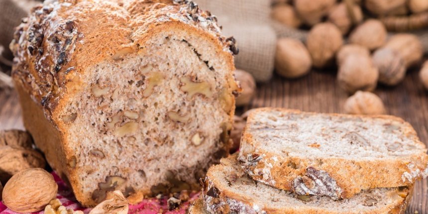 Auf einem dunklen Holztisch liegt ein aufgeschnittenes Kastenbrot mit Walnüssen im Teig, daneben liegen einzelne Scheiben und ganze Walnüsse.. Artikel "Nussbrot ist das Brot des Jahres 2025" öffnen.