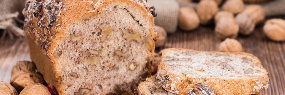 Auf einem dunklen Holztisch liegt ein aufgeschnittenes Kastenbrot mit Walnüssen im Teig, daneben liegen einzelne Scheiben und ganze Walnüsse.