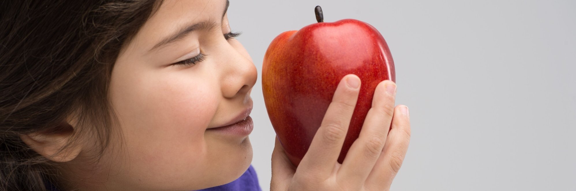 Ein Mädchen riecht an einem Apfel.