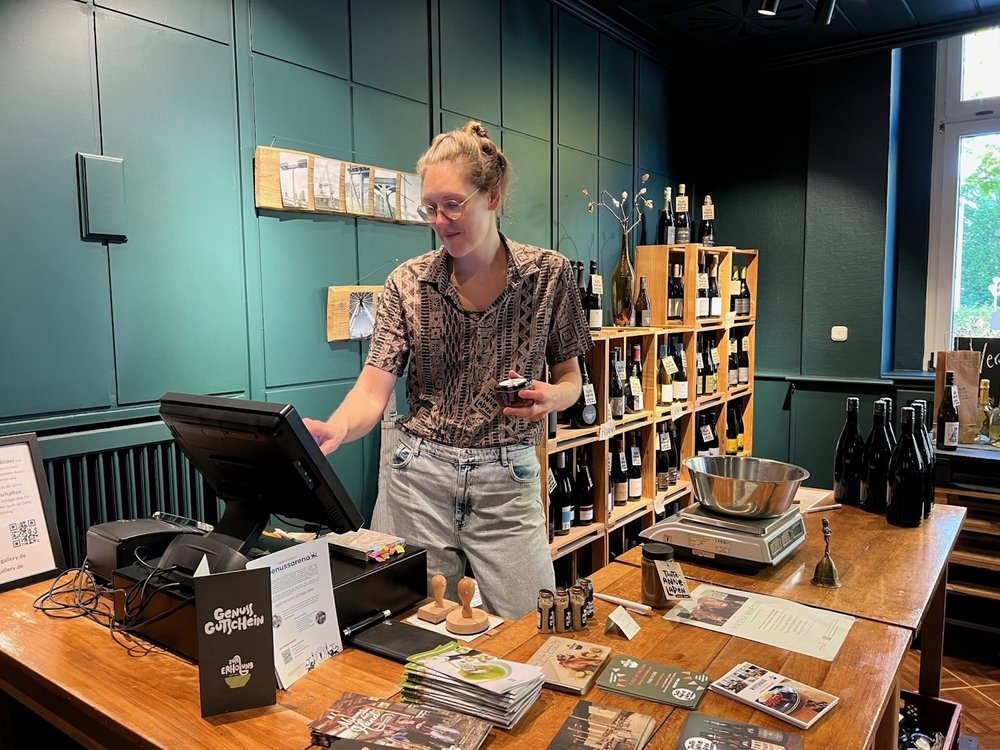 Eine Frau steht in einem Laden und tippt den Preis in eine Kasse ein.