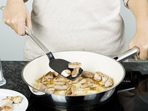 Eine Person brät Fleisch in Pfanne.