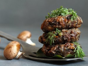 Ein Stapel aus drei Frikadellen auf einem Löffel. Daneben liegen drei Pilze.