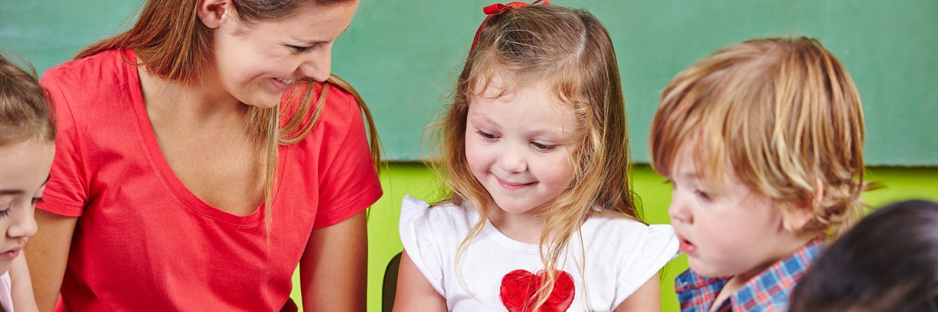 Eine Erzieherin sitzt mit Kita-Kindern am Tisch und malt. 