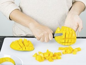Eine Person schneidet Mangoschale in Würfel.