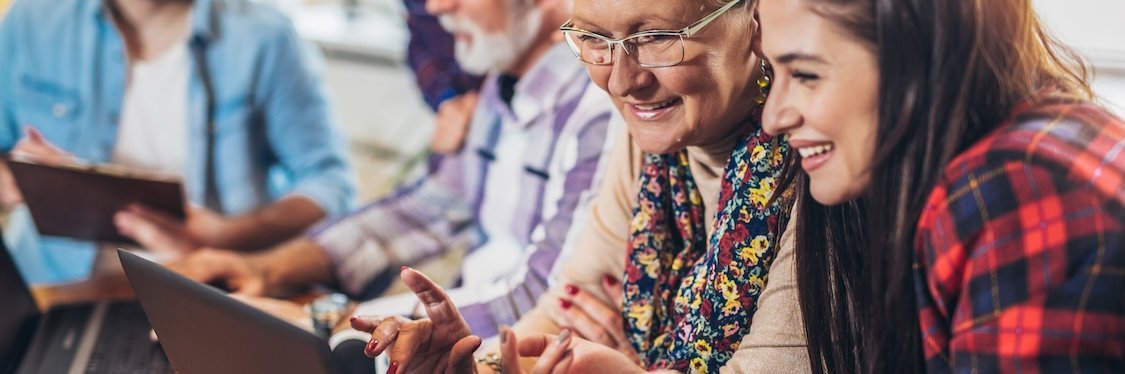 Eine altersgemischte Lerngruppe Erwachsener arbeitet an Laptops.