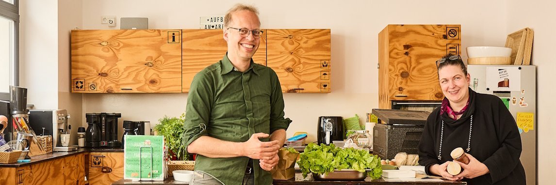 Ein Mann und eine Frau stehen in einer Küche und lächeln in die Kamera.