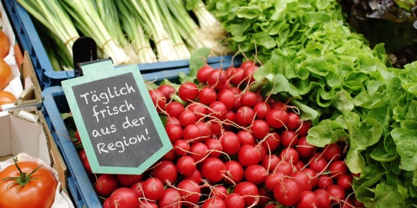 In Gemüsekisten liegen Tomaten, Radieschen, Lauchzwiebeln und Salatköpfe dazu ein Schild mit der Aufschrift: Täglich frisch aus der Region.. Artikel "Nachhaltigkeit im Supermarkt" öffnen.