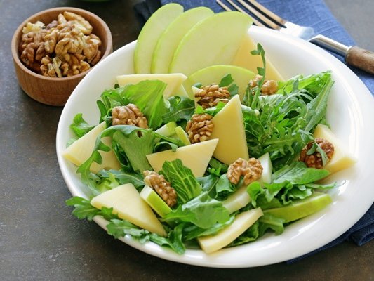 Ein grüner Salat mit Apfelscheiben und Walnusskernen in einer weißen Schale.