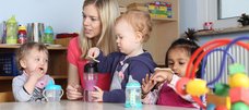 Erzieherin spricht mit trinkenden Kleinkindern am Tisch