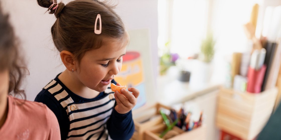 Ein Kind in einer Kitagruppe isst eine Mandarine.. Artikel "Schmecken lernen" öffnen.