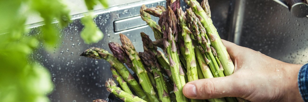 Hand wäscht grünen Spargel im Waschbecken.