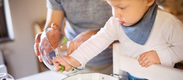 Kleinkind füllt mit Hilfe eines Erwachsenen Spinatblätter in ein Abtropfsieb