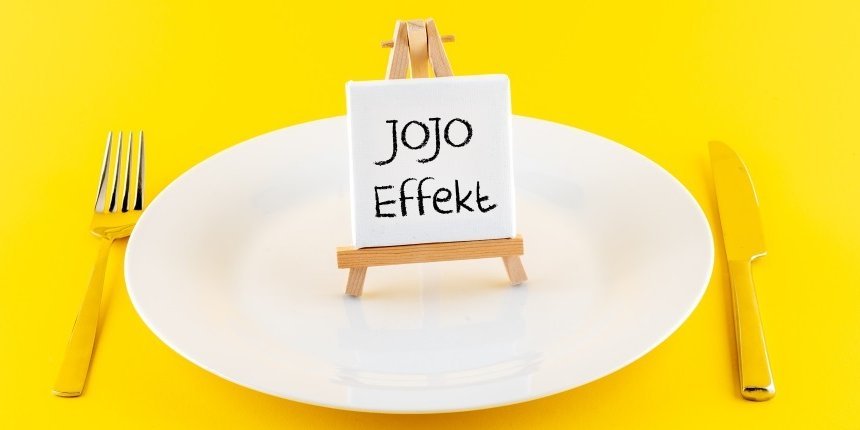 Auf einem gelben Untergrund steht ein weißer Teller, daneben liegt Besteck. Auf dem Teller steht eine Mini-Staffelei mit einem Schild mit der Aufschrift „Jojo-Effekt“.. Artikel "Die Biologie hinter dem Jo-Jo-Effekt" öffnen.