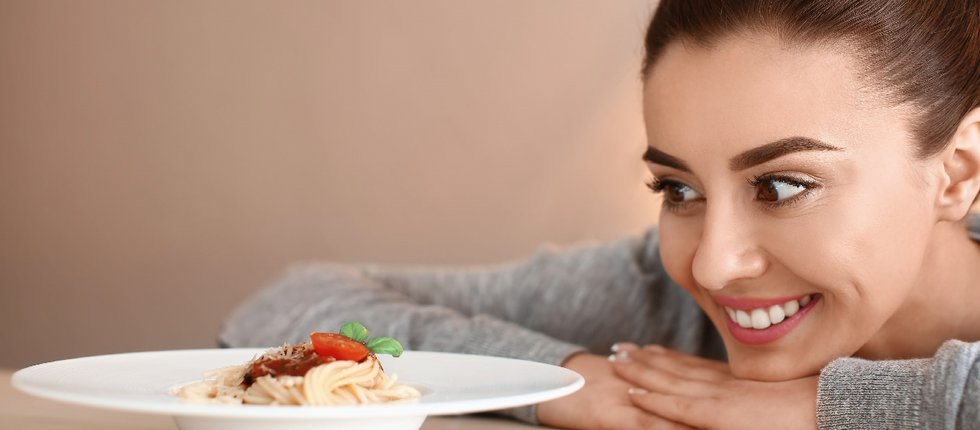 Eine Frau hat ihr Kinn auf die Arme gelegt und schaut auf einen weißen Teller mit Spaghetti