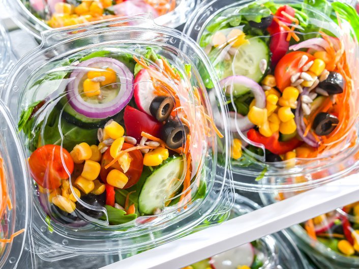 Verzehrfertige Salatmischungen in Plastikschalen liegen im Kuehlregal.