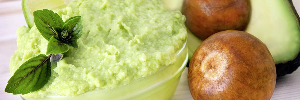 Eine Schale mit Avocadomus steht neben einer aufgeschnittenen Avocado.