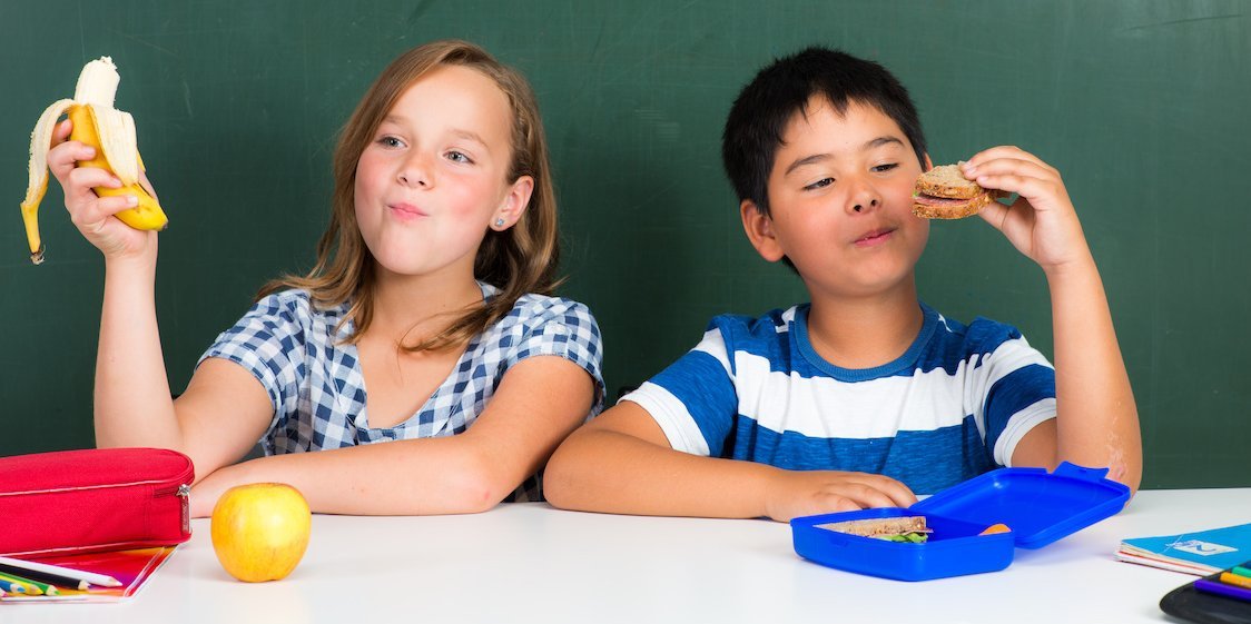 Zwei Schulkinder sitzen vor einer Tafel und essen ein Brot und eine Banane.. Artikel "Mein Frühstück für unsere Zukunft" öffnen.