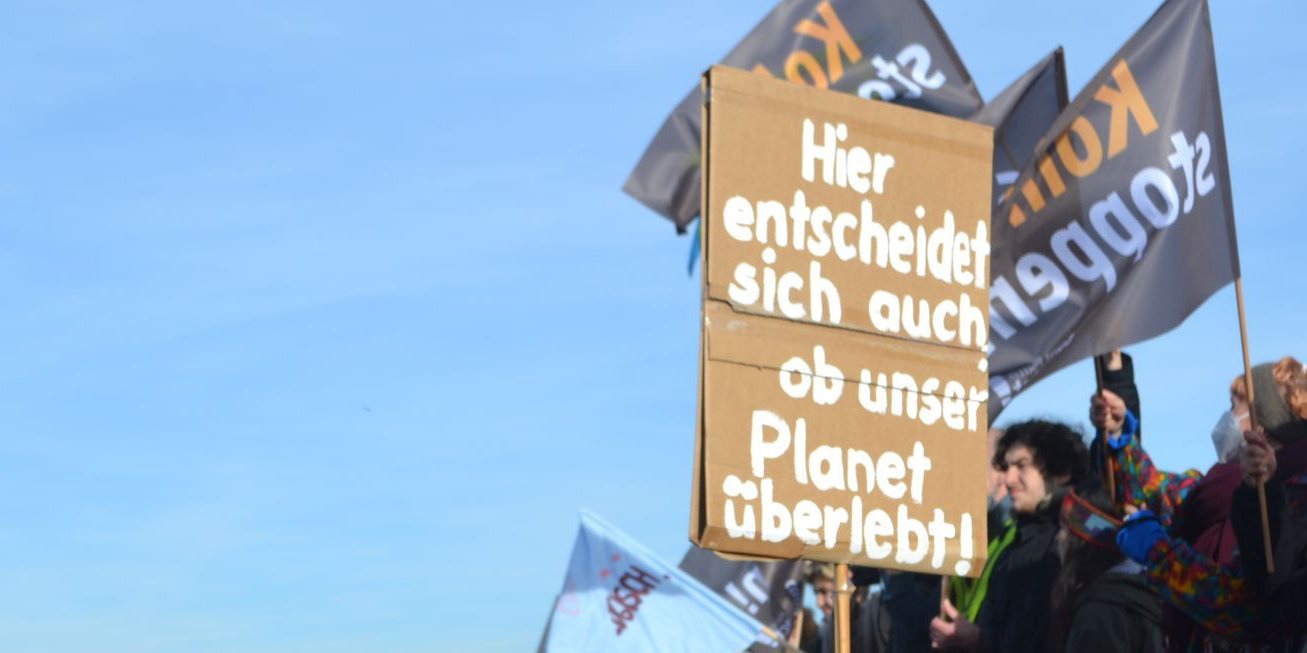 Schild auf einer Demonstration am Rand einer Kohlegrube in Lützerath mit der Aufschrift "Hier entscheidet sich auch, ob unser Planet übelebt".  . Artikel "Planetary Health – Basis unseres Ernährungssystems" öffnen.