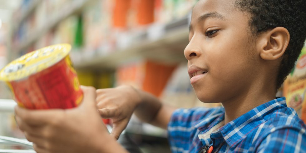 Junge schaut sich im Supermarkt ein Lebensmitteletikett an.. Artikel "Was ist drin im fertig verpackten Lebensmittel?" öffnen.