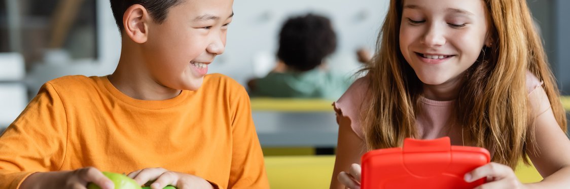 Zwei offensichtlich gut gelaunte Schulkinder öffnen ihre Brotdosen.