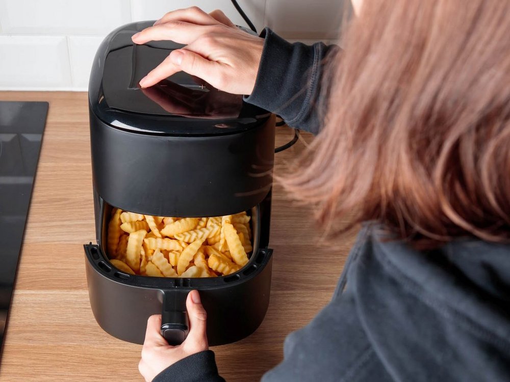 Eine Frau öffnet die Schublade einer Heißluftfritteuse in der Pommes liegen.