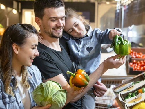 Eine junge Familie wählt im Supermarkt Gemüse aus.