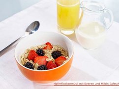 Schale mit Haferflocken und Beeren, Löffel, Glas Orangensaft und einen Krug mit Milch.