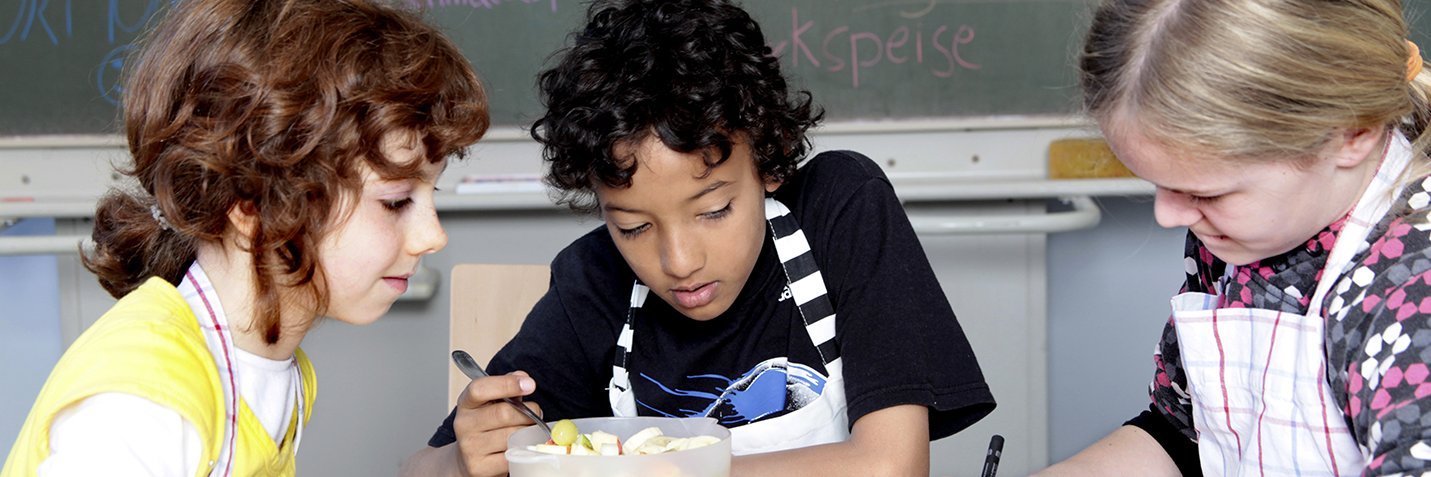 Drei Kinder schneiden im Klassenzimmer Obst.