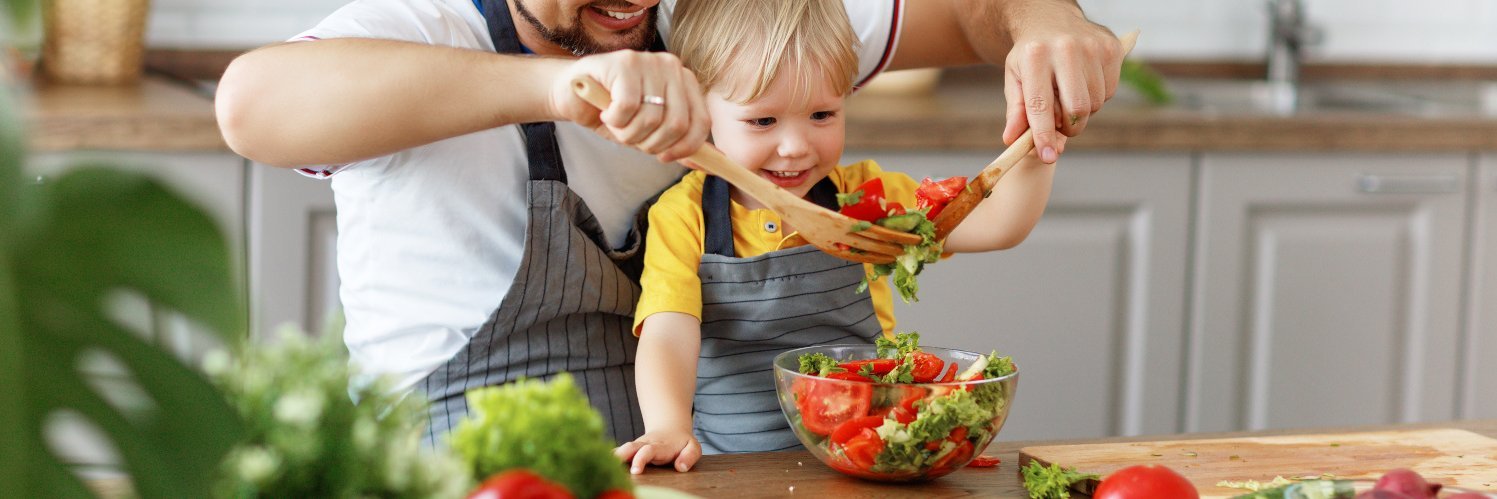Vater und Sohn mischen zusammen Salat in einer Schüssel.