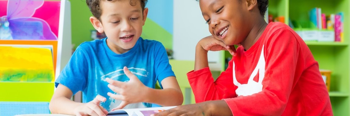 Zwei Jungen in einer Kita sitzen am Tisch und schauen sich ein Buch an.