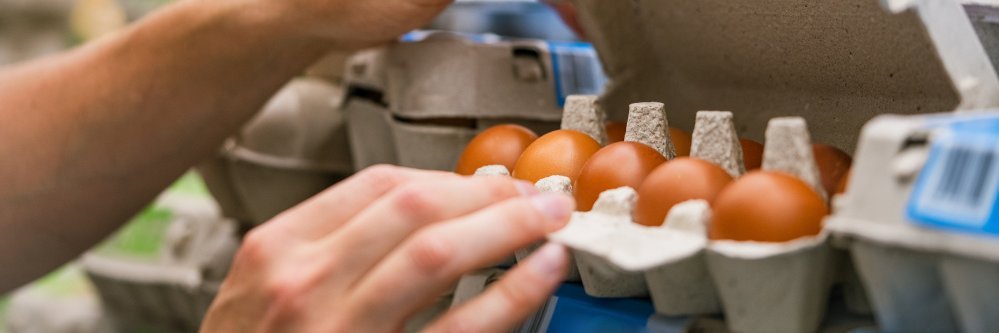 Person öffnet Eierkarton im Supermarktregal.