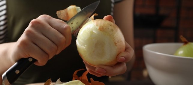 Eine Frau schält mit einem Küchenmesser eine große Zwiebel. 