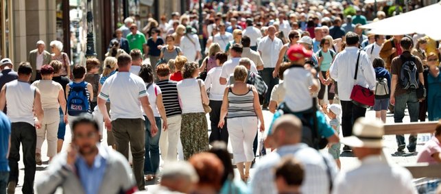 Viele Menschen gehen in einer Stadt durch die Fußgängerzone.