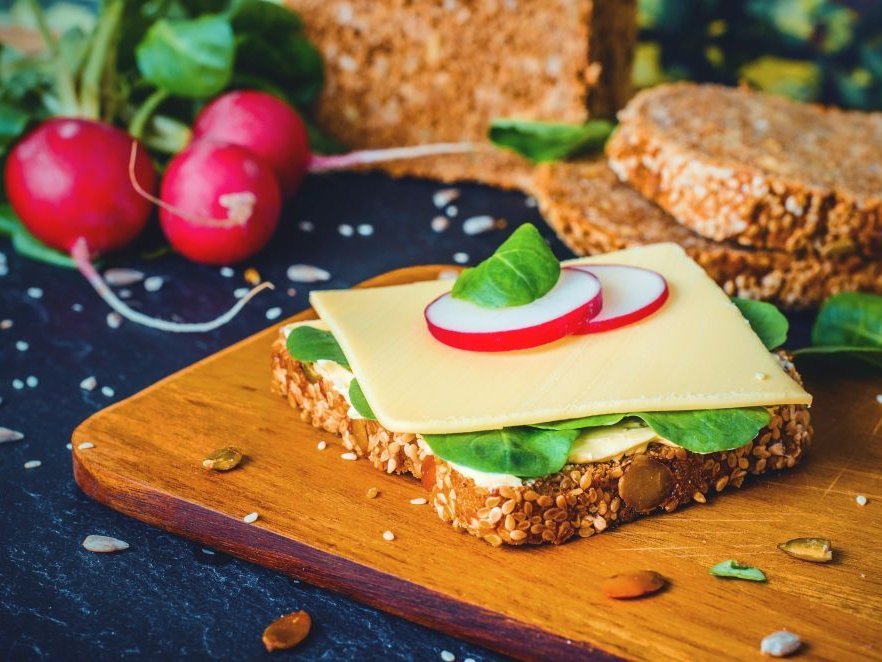 Ein Käsebrot mit Salatblatt und Radieschenscheiben auf einem Holzbrett.