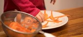 Kinderhand greift gehobelte Karotte von einem Teller und gibt sie in ein Sieb.